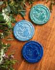 This round Michigan Trivet Tile features the outline of the state's two peninsulas including some of the larger northern islands of Michigan. To the left of the design reads "The Great Lakes State" and surrounding it, in a border, reads the word Michigan four times.