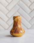 Sunstone Snowdrop vase, gleaming in bright iridescent yellow, pink, and orange tones set on white marble with a herringbone Pewabic tile pattern in a matte, white glaze.
