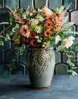 Glossy, deep green Balsam Pinecone vase with blush-pink and vibrant green flowers against an Aurora Iridescent tile wall.