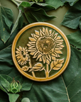 A two-tone glossy, round Sunflower Trivet with golden border and outline set against an emerald green background.