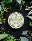 A Mooncake Paperweight in our glossy Celadon glaze, surrounded by cool greenery and delicate concord grapes.