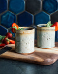 Two ceramic Rocks Cups in a glossy Frost glaze with mint and strawberries on a wooden cutting board against a blue tiled wall.