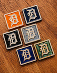 Set of six 4x4 Old English D tiles in various glaze colors arranged on a warm wooden surface.