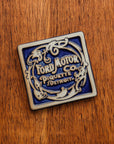 Ford Motor Co. Piquette logo tile on a warm wooden background.