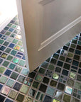 A blend of blue and green tiles in a range of textures and glazes on the floor at the entryway of a home. The door is slightly ajar, welcoming you into the space.