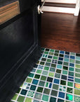 A blend of blue and green tiles in a range of textures and glazes on the floor at the entryway of a home. The door is slightly ajar, welcoming you into the space.