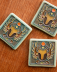 This hand painted tile features a scarab is multiple brown colors on a background of the crystalline, shimmering deep green Viridian glaze with a pale blue border.