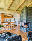 A quarter view of a three-sided custom Pewabic Tile fireplace with a strong geometric pattern of subway and custom-cut tiles. The client’s furniture, including their dining table and cow-hide lounge chair are visible in the frame.