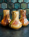 Three Snowdrop vases in Sunstone iridescent, with a marbled design on a dark slate surface, set against a patterned green tile background.