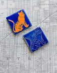 Two ceramic 3x3 Tigers tiles, both hand-painted and single-glazed, on a Detroit map background.