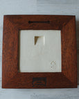 The back of the framed piece is pictured showing the open-back structure of the frame. This exposes the Pewabic Stamp one the back of the tile. There is a burned on stamp of the woodworker who created the frame- it says "Handcrafted Family Woodworks".