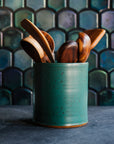 Floral arrangement in a freckled Greenstone vase with teakwood utensils against an Aurora Iridescent tile wall. 