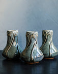 Three glossy, deep green Balsam Snowdrop vases against a dark-grey, lime-washed wall. 
