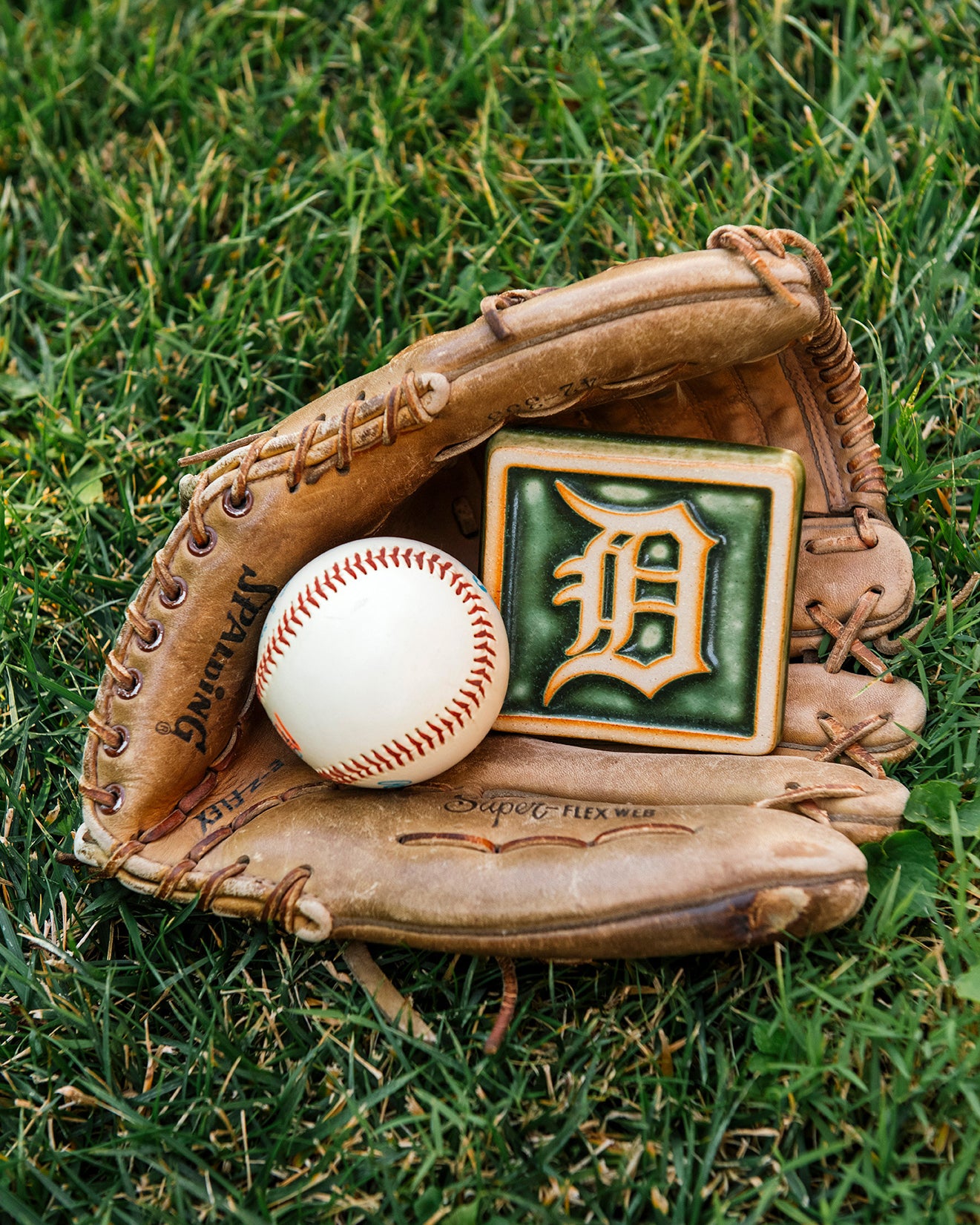 Baseball glove with a baseball and a 4x4 Old English D tile in Ivy/Natural on grass.