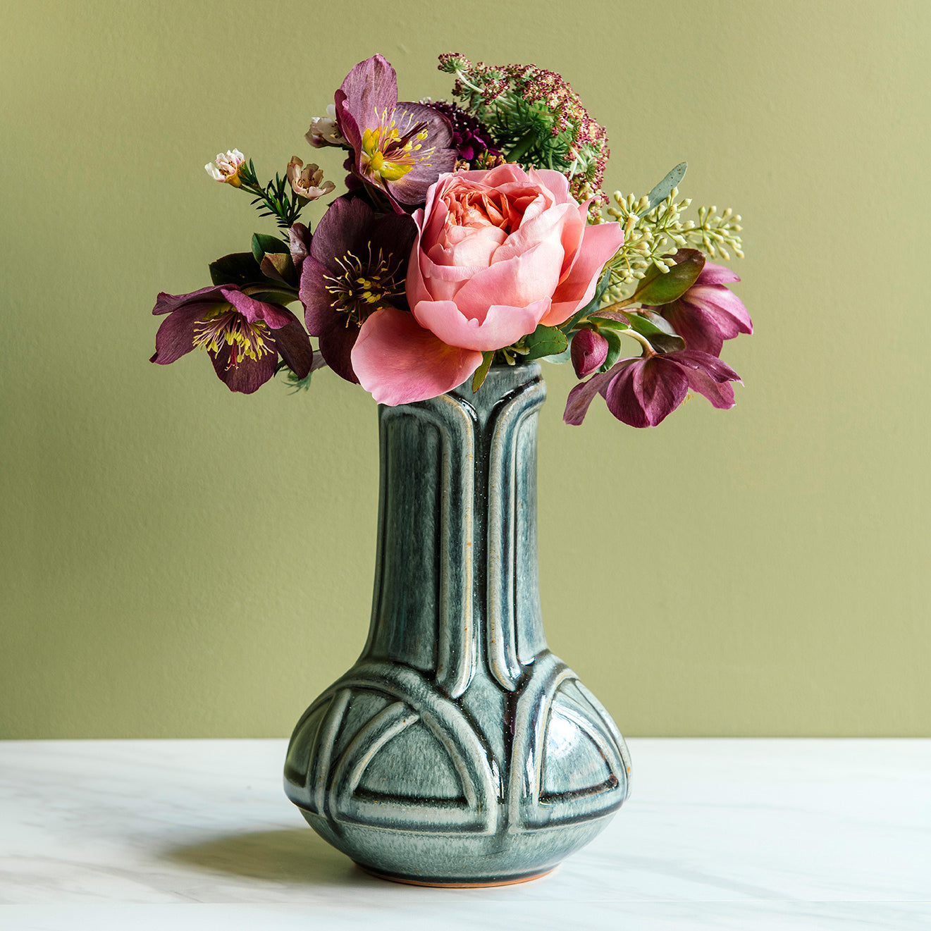Glossy, green, Balsam Vase with a vibrant bouquet set on white marble with a light green background. 