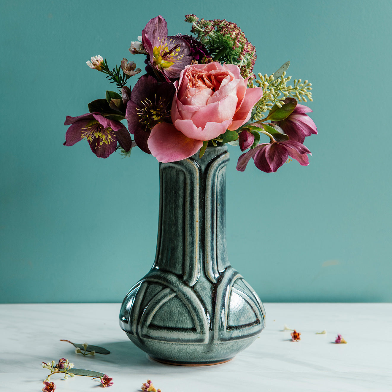 Glossy, green, Balsam Vase with a vibrant bouquet set on white marble with a bright teal background. 