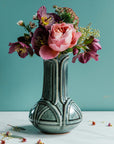 Glossy, green, Balsam Vase with a vibrant bouquet set on white marble with a bright teal background. 