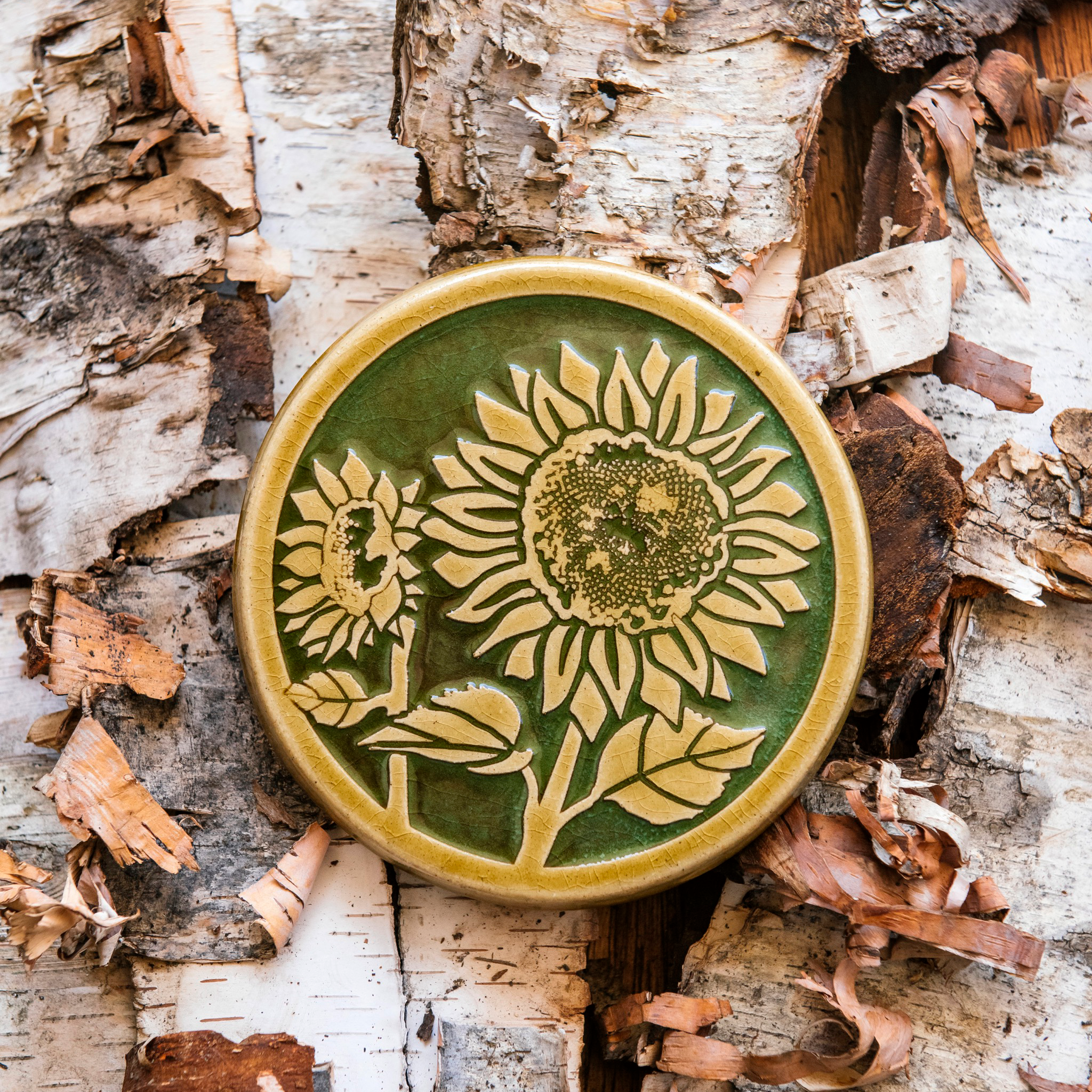 A two-tone glossy, round Sunflower Trivet with golden border and outline set against an emerald green background. 