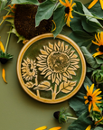 A two-tone glossy, round Sunflower Trivet with golden border and outline set against an emerald green background. 