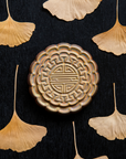 A Mooncake Paperweight in shimmering Blush Iridescent surrounded by dried ginkgo leaves. 