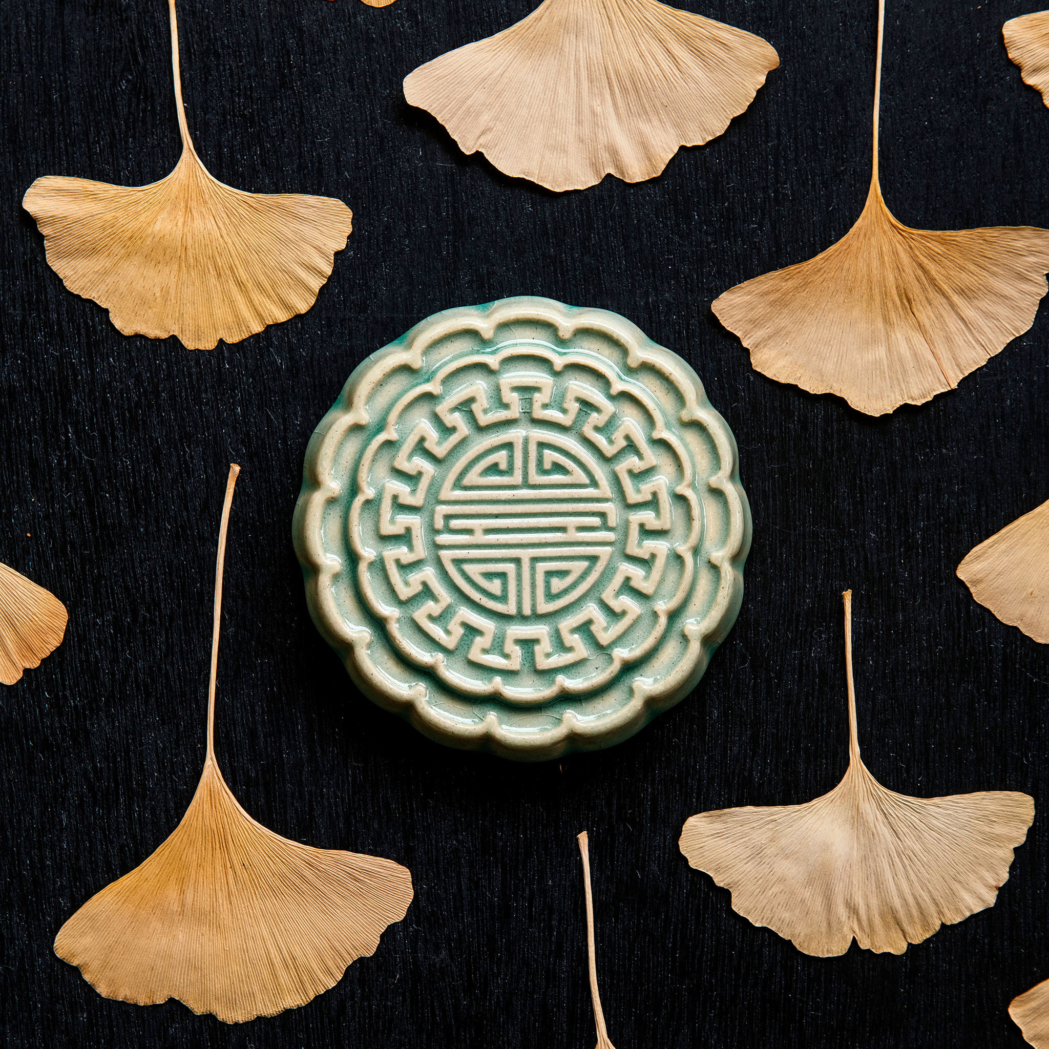 A Mooncake Paperweight in our glossy Celadon glaze, surrounded by dried ginkgo leaves.