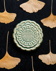 A Mooncake Paperweight in our glossy Celadon glaze, surrounded by dried ginkgo leaves.