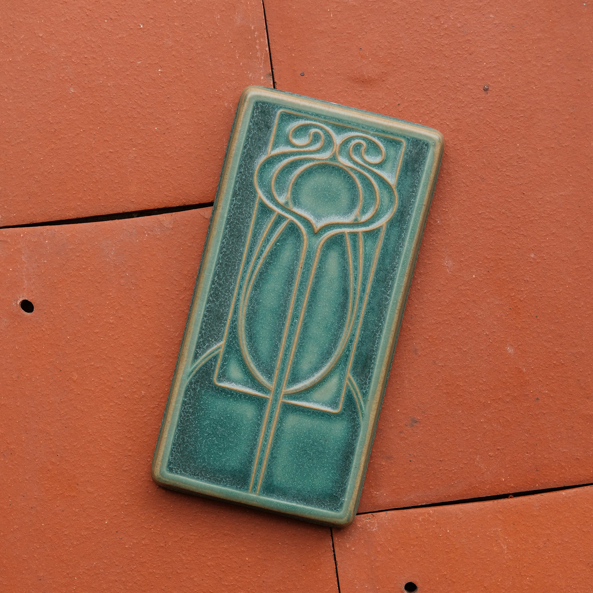This vertical rectangle tile has an abstract low relief design. Interconnecting hard and curved lines come together to create a craftsman style motif.