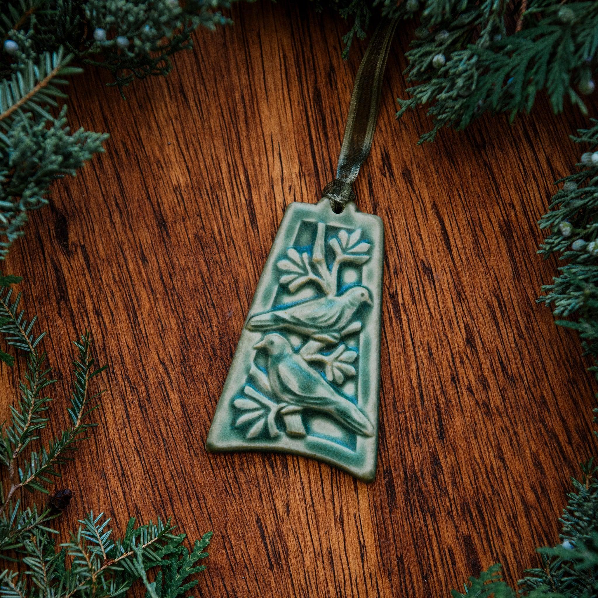 The bell-shaped Two Turtle Doves Ornament features two doves siting on the branches of a leafy tree.