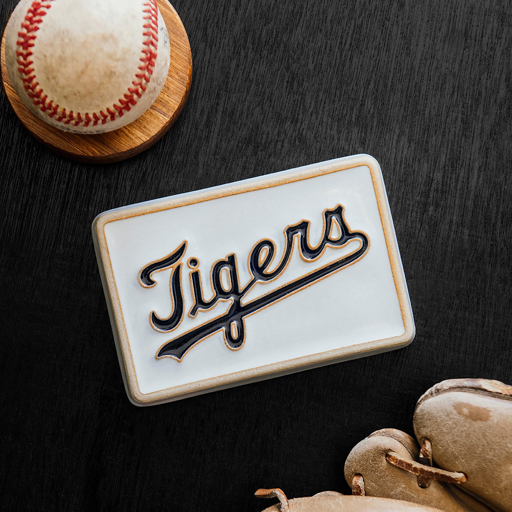 Baseball, baseball glove, and 'Tigers' logo tile on a dark wood surface. 