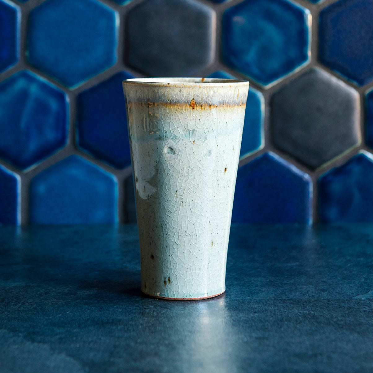 A ceramic Pewabic Pint in a glossy Frost glaze against a blue hex tile background. 