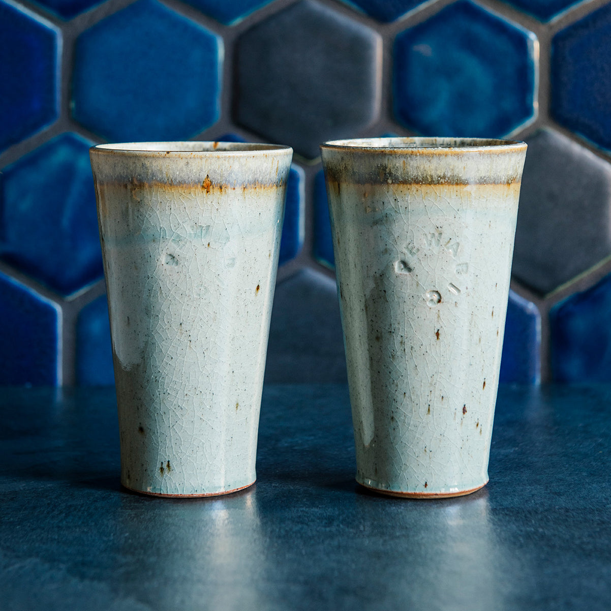 Two ceramic Pewabic Pints in a glossy Frost glaze against a blue hex tile background. 