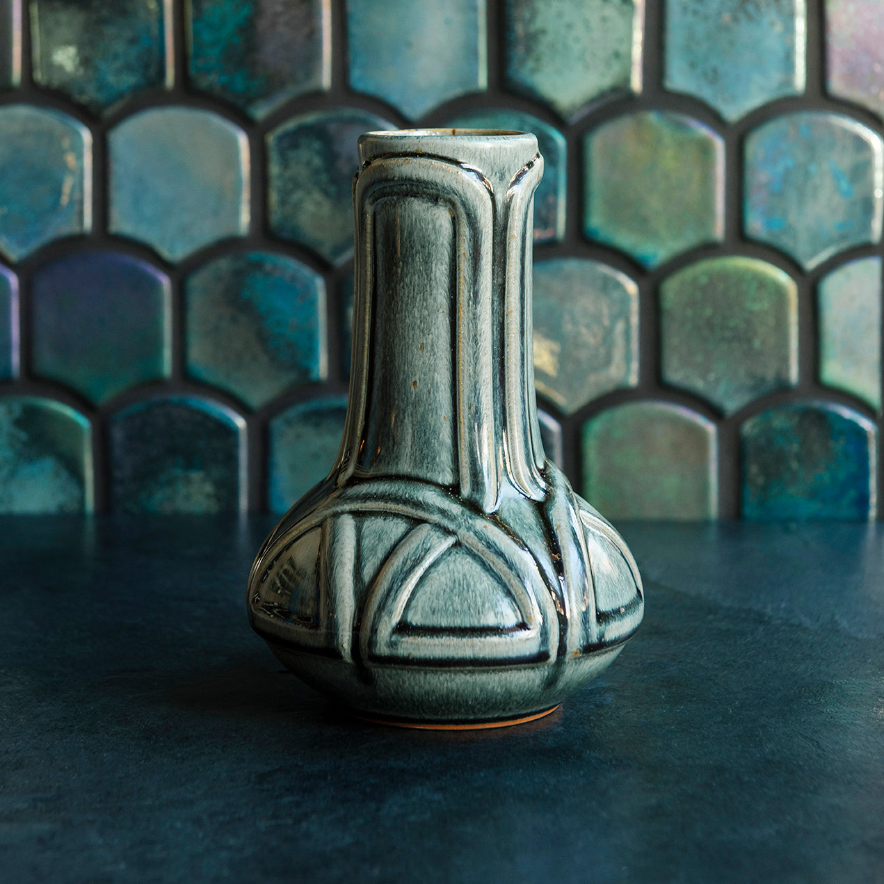 A glossy green Balsam Celtic Vase against an Iridescent fishscale tile background.