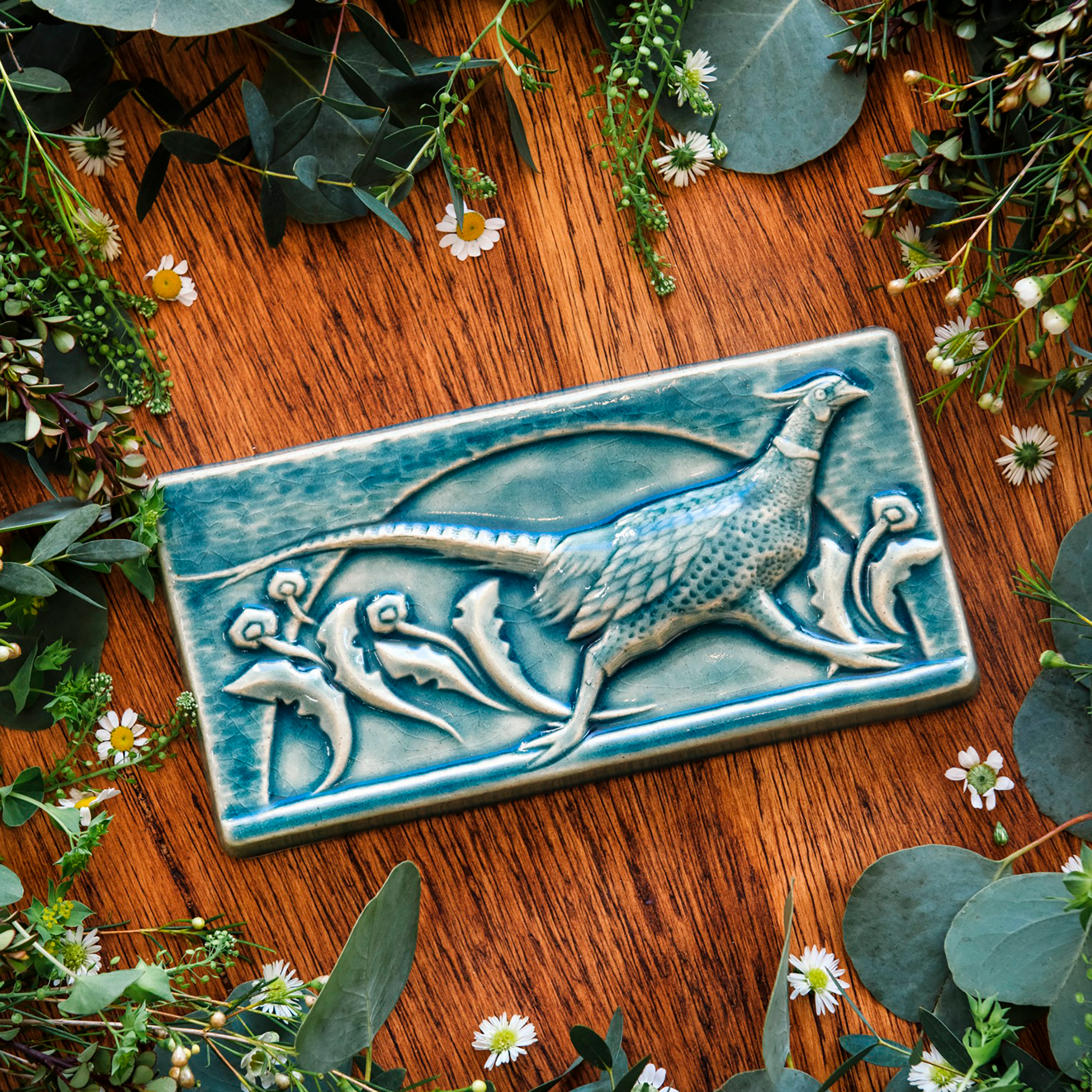 This hand-sculpted tile features a pheasant running through a field of dandelions. It is featured in a glossy blue Glacier glaze. 