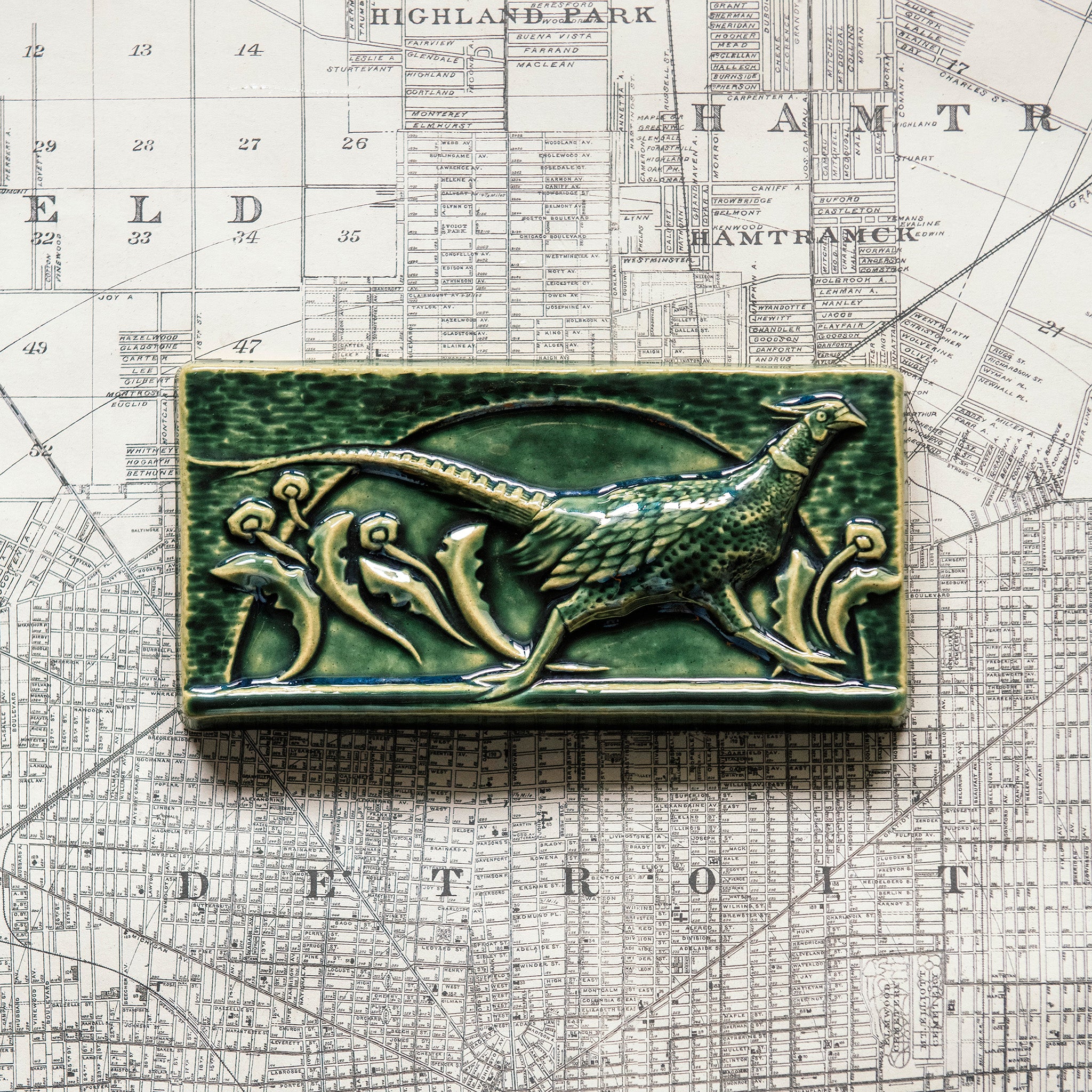 This hand-sculpted tile features a pheasant running through a field of dandelions. It is featured in a glossy green Kale glaze. 