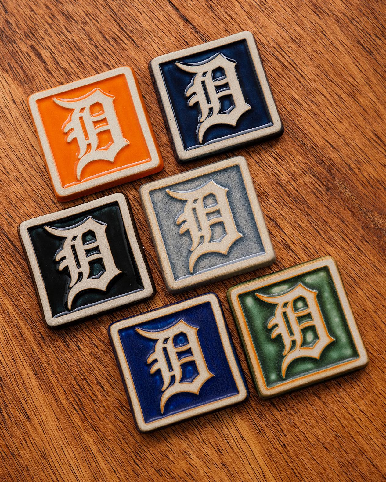 Set of six 4x4 Old English D tiles in various glaze colors arranged on a warm wooden surface. 