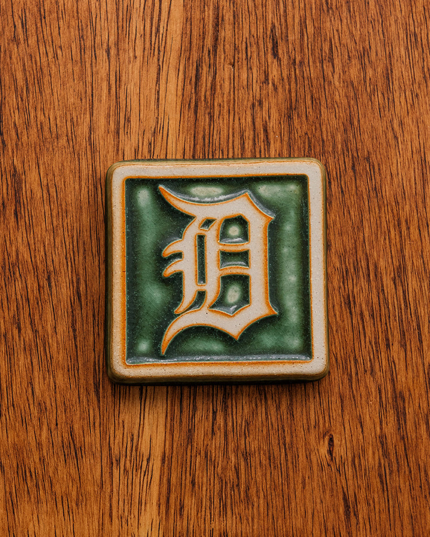 4x4 Old English D tile in Ivy/Natural on a warm wooden surface.