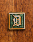 4x4 Old English D tile in Ivy/Natural on a warm wooden surface.