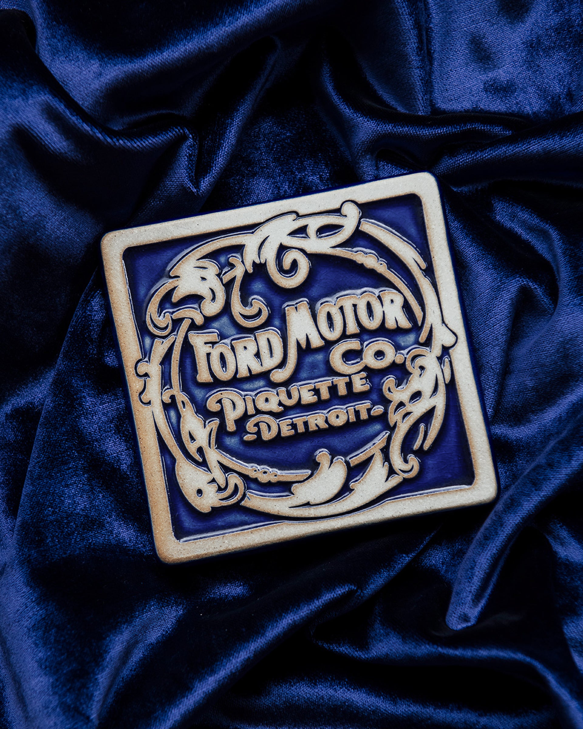 Ford Motor Co. Piquette logo tile on a blue velveteen fabric background. 
