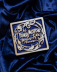 Ford Motor Co. Piquette logo tile on a blue velveteen fabric background. 