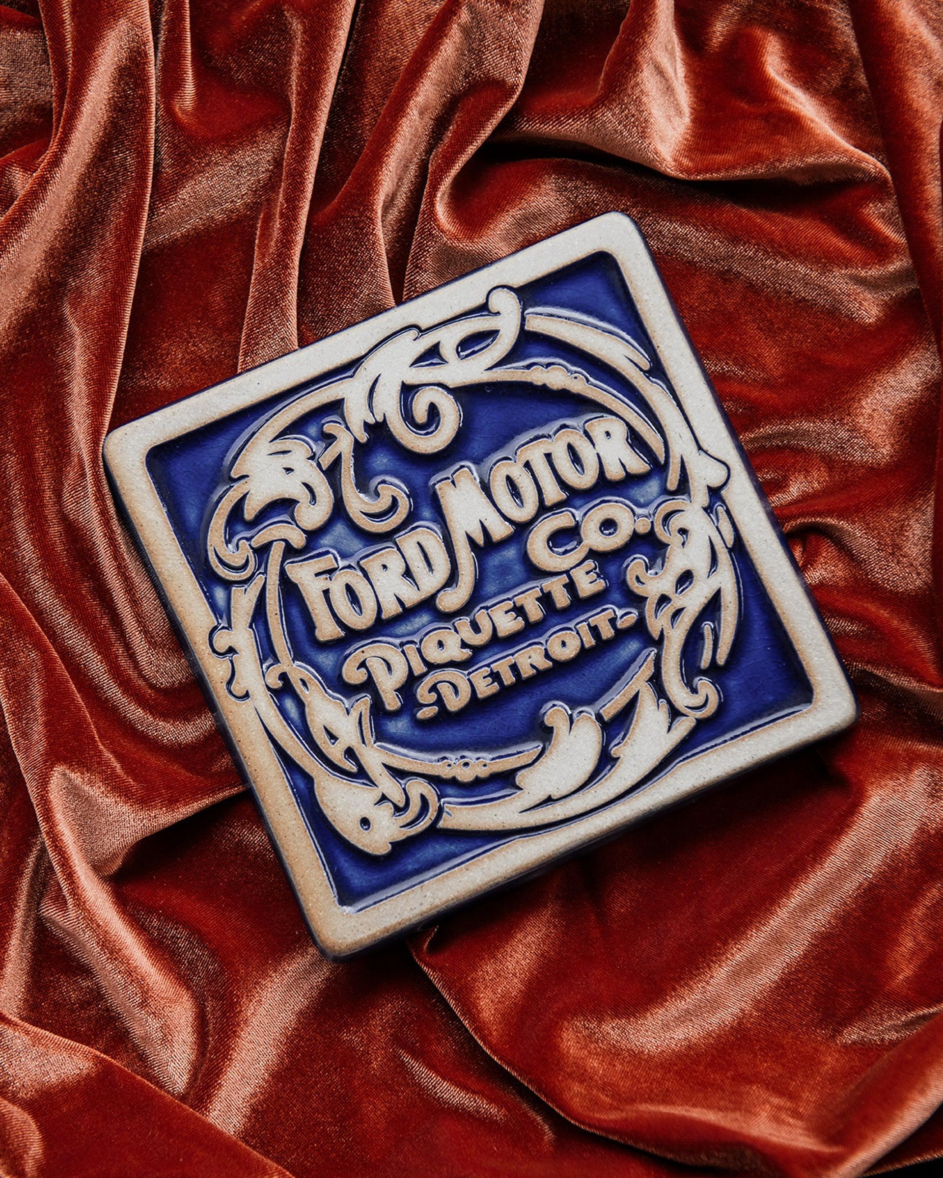 Ford Motor Co. Piquette logo tile on an orange velveteen fabric background. 