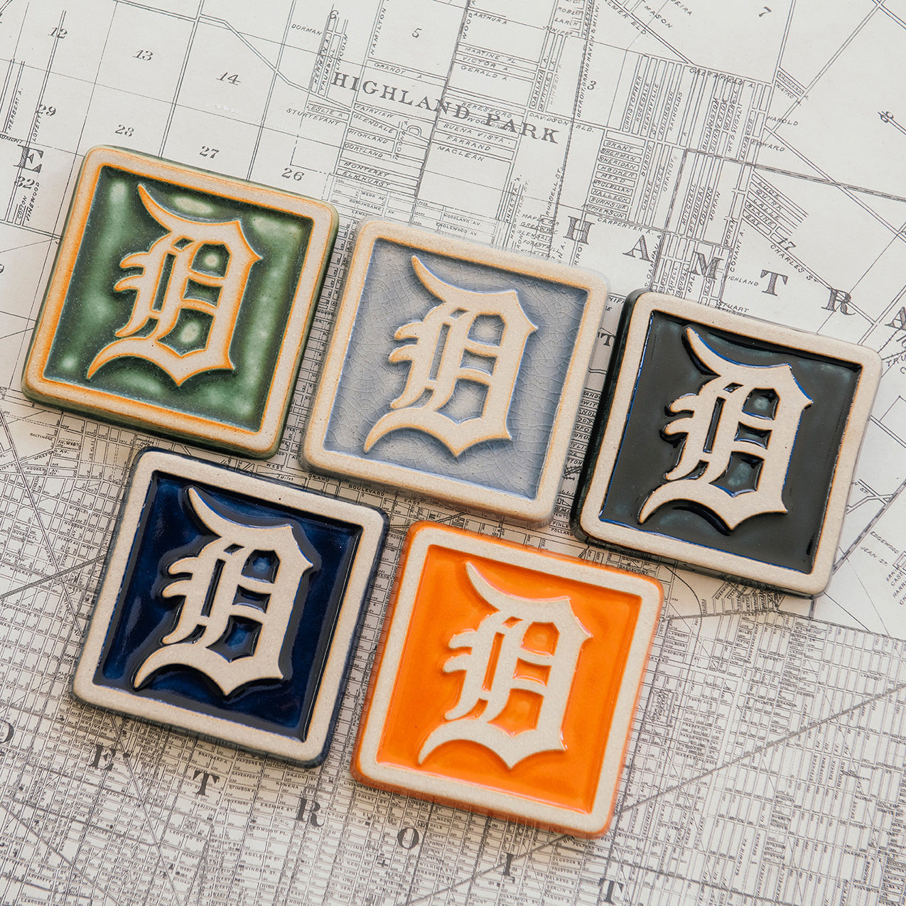 Set of five 4x4 Old English D tiles in various glaze colors arranged on a Detroit map.