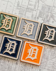 Set of five 4x4 Old English D tiles in various glaze colors arranged on a Detroit map.