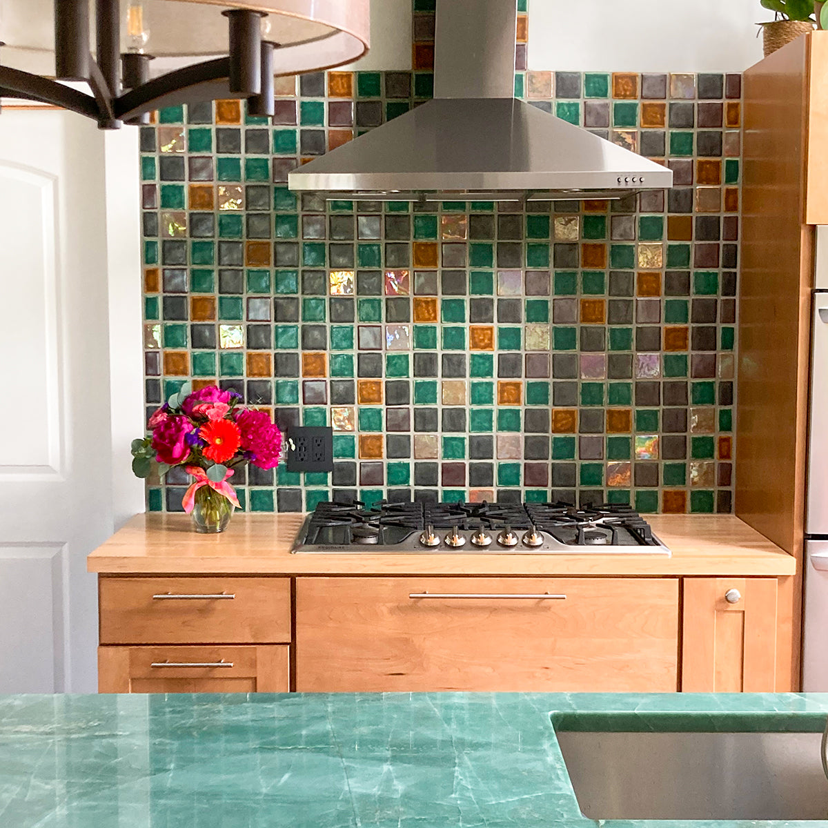 Multicolored tile backsplash in a kitchen with modern cabinets and a jade green countertop