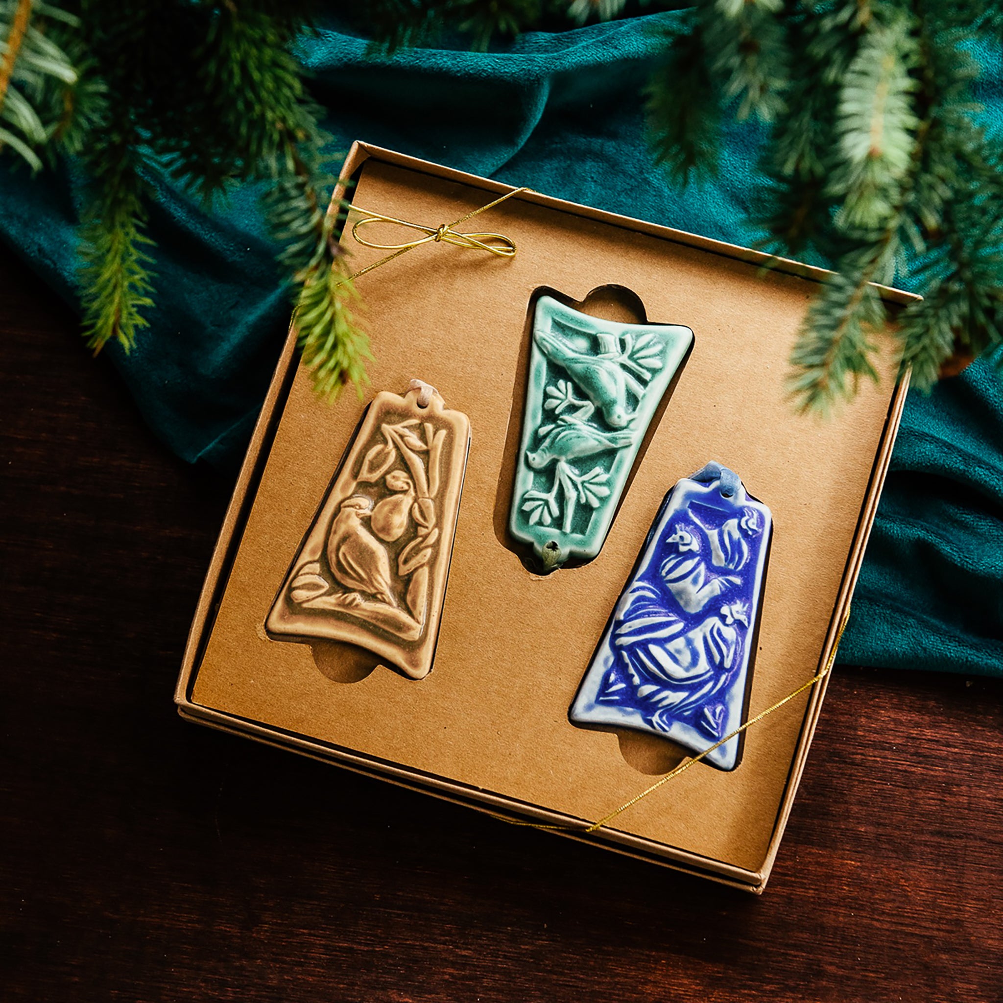 Three ceramic ornaments are sitting in a gift box and placed under a Christmas tree.
