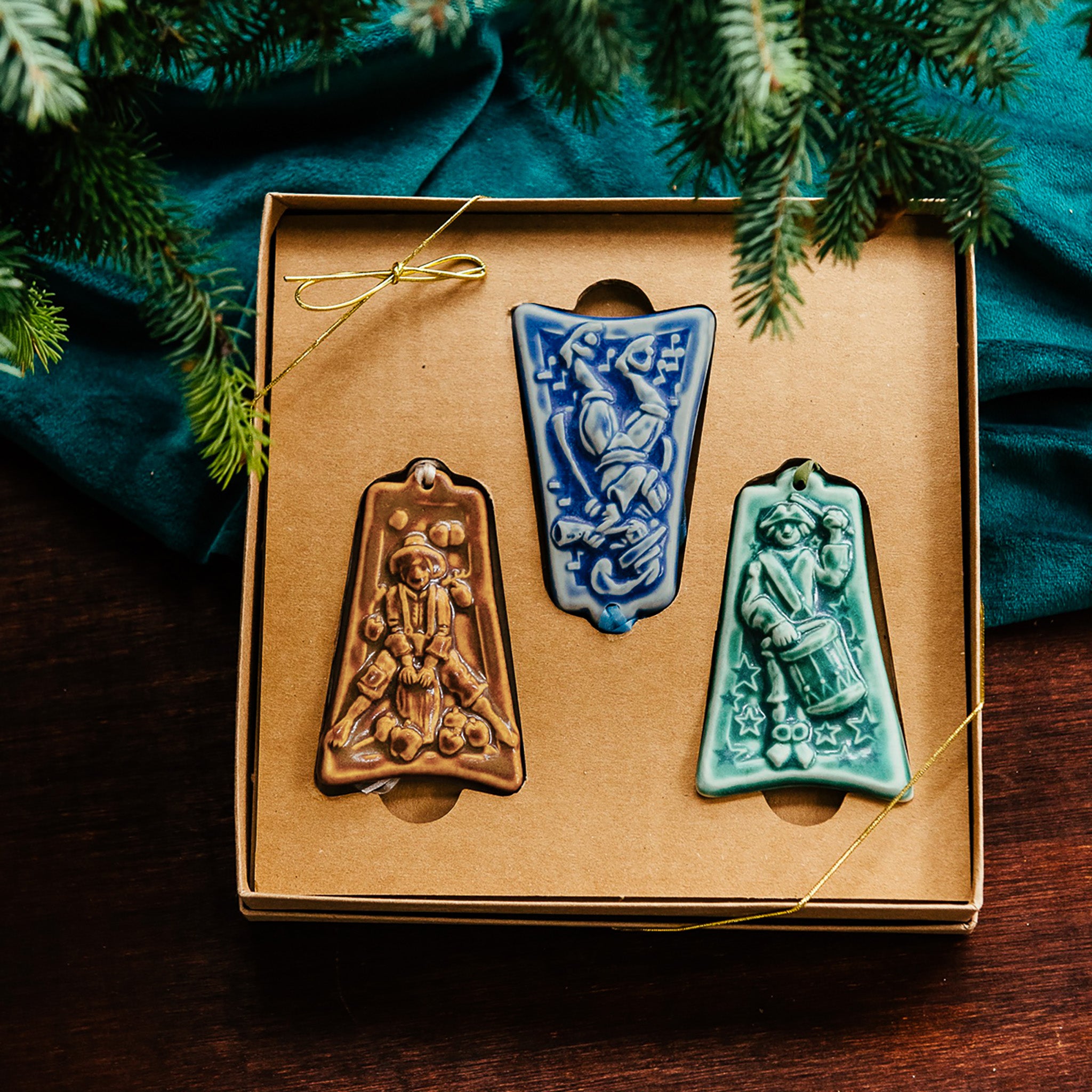 Three ceramic ornaments are sitting in a gift box and placed under a Christmas tree.