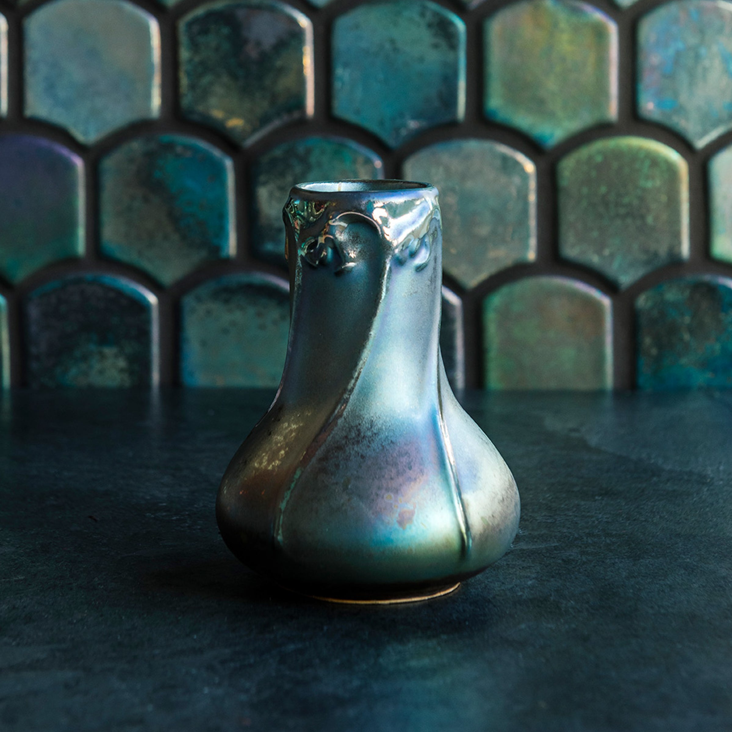 Matte Green Iridescent Snowdrop vase on a dark slate foreground and green, tilled background.