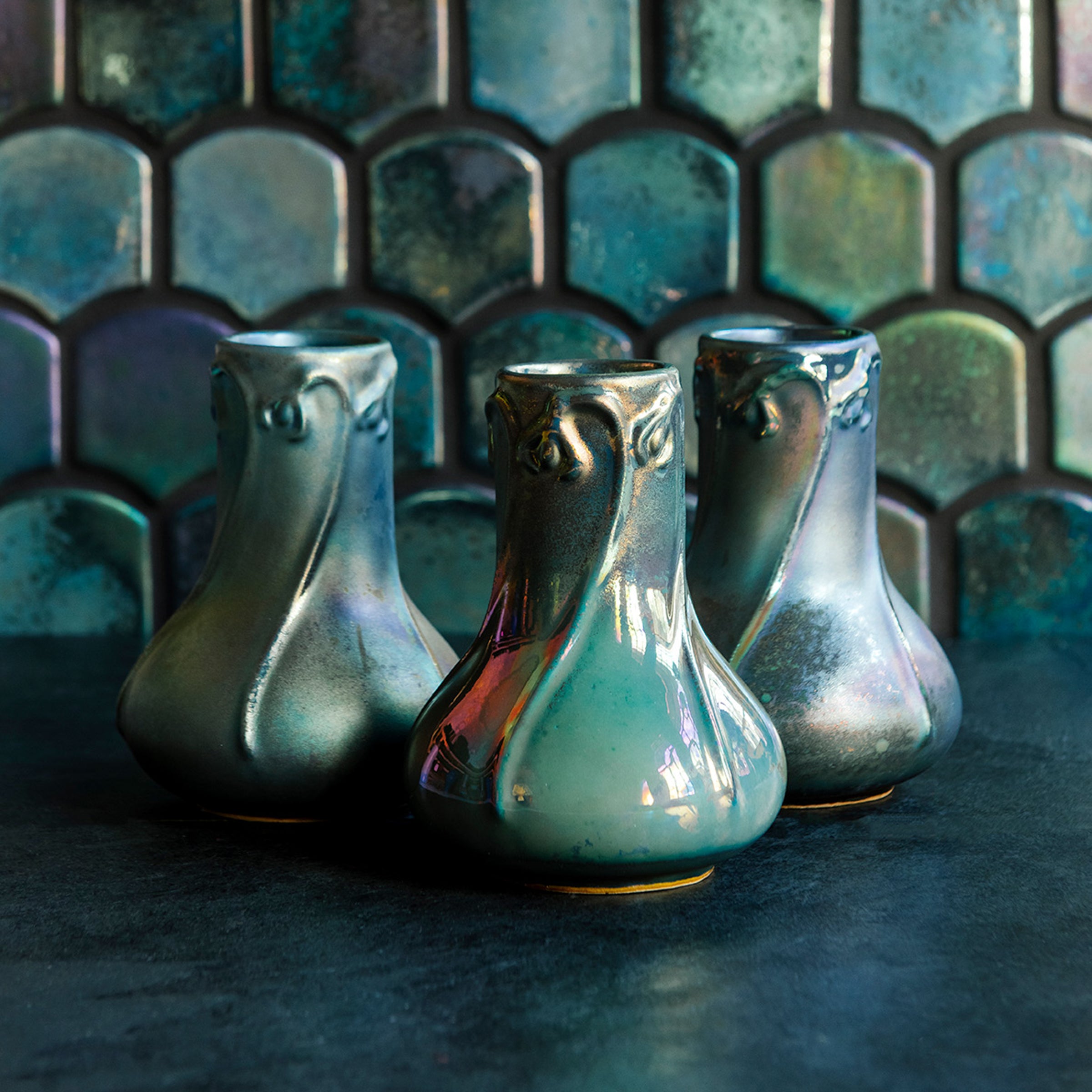 Three Matte Green Iridescent Snowdrop vases on a dark slate foreground and green, tilled background.