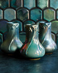 Three Matte Green Iridescent Snowdrop vases on a dark slate foreground and green, tilled background.