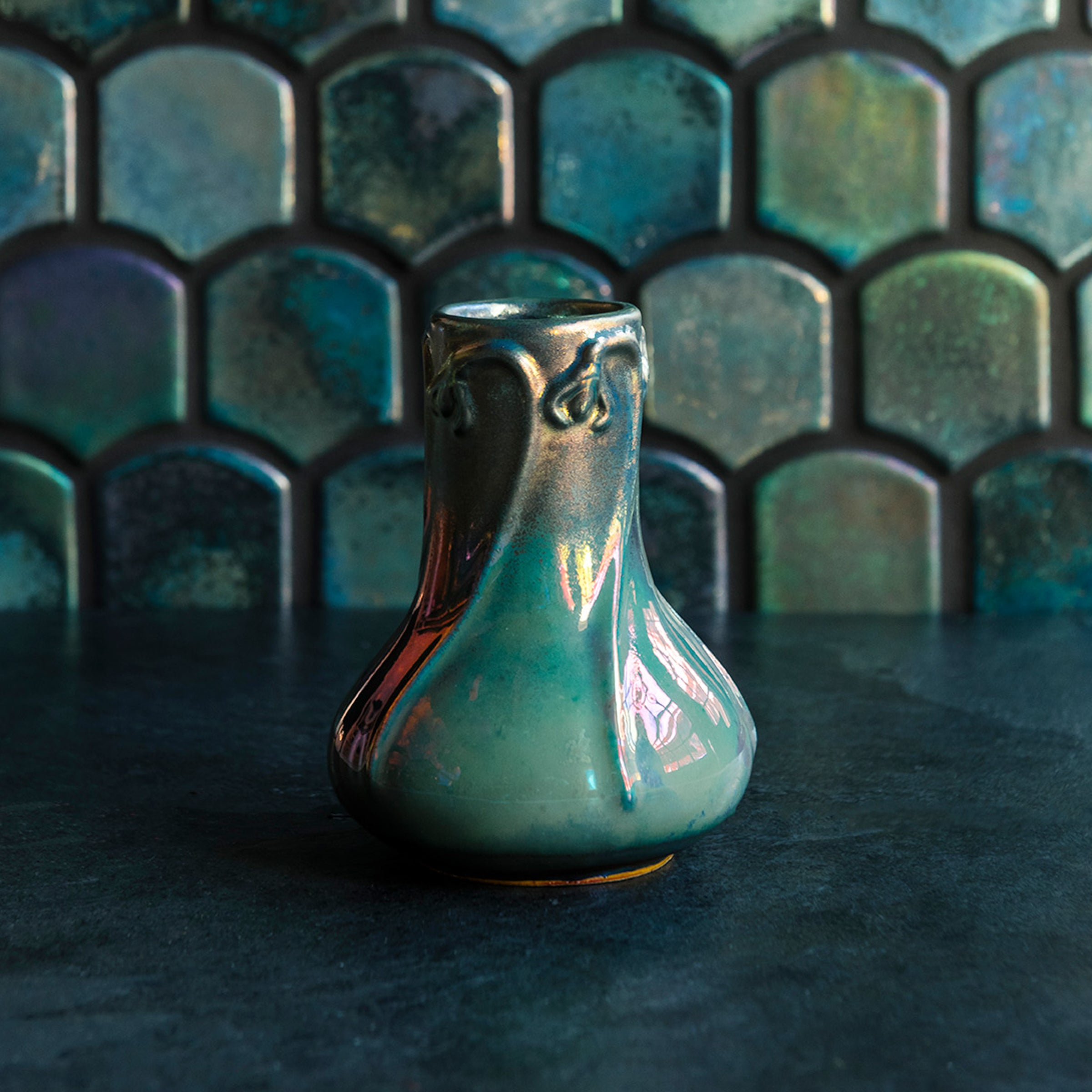 Matte Green Iridescent Snowdrop vase on a dark slate foreground and green, tilled background.