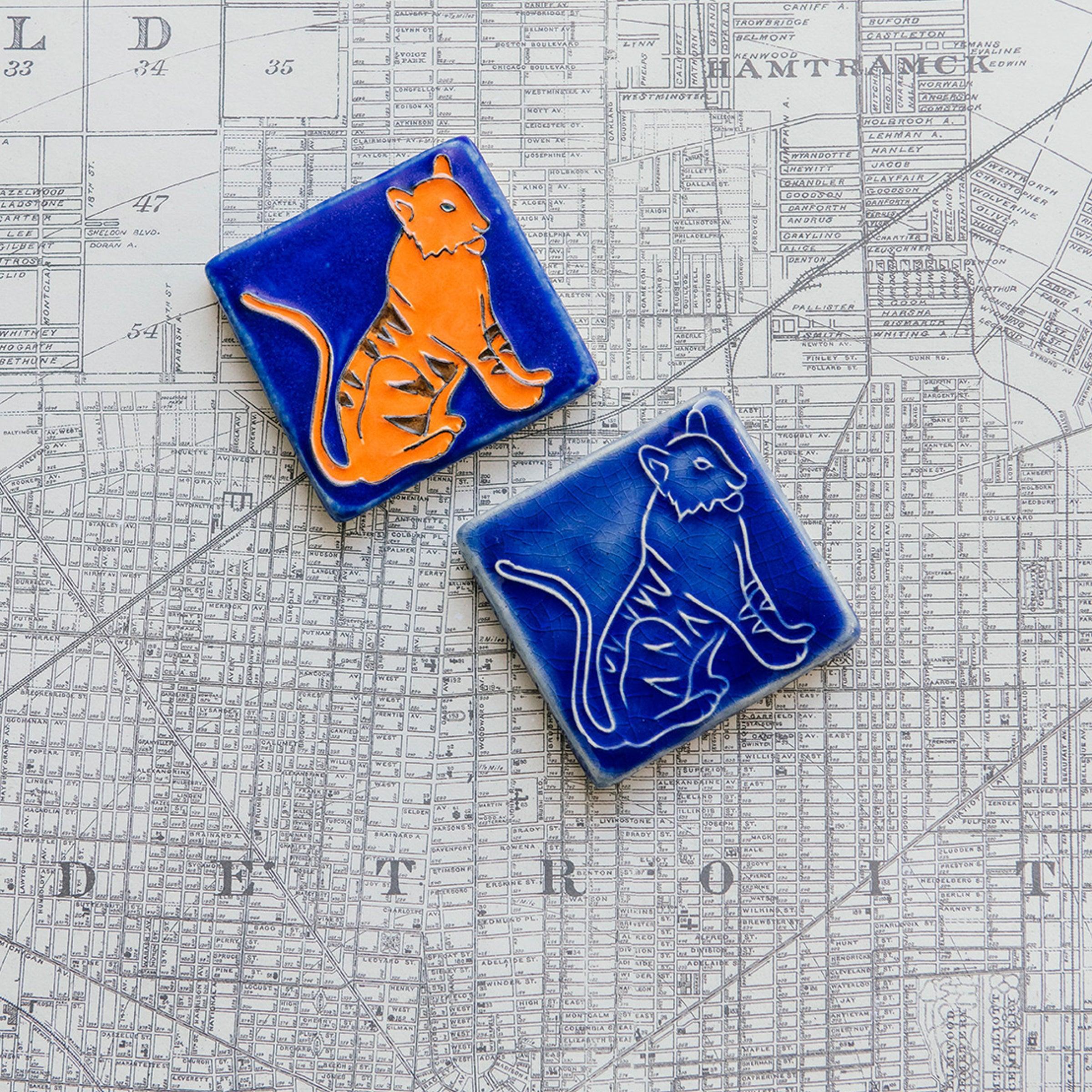 Two ceramic 3x3 Tigers tiles, both hand-painted and single-glazed, on a Detroit map background.